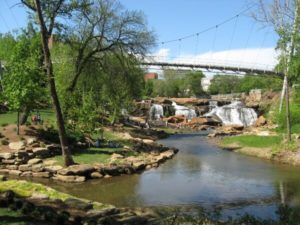 Waterfall under suspension bridge with trees on the shore.