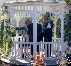 Bride, groom, & preacher in garden gazebo on sunny day