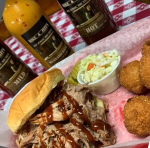 Pulled pork sandwich with sauce bottles , hush puppies, and slaw