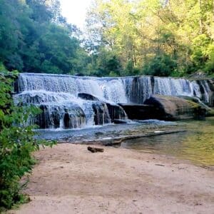 Cascading waterfall by sandy shore.