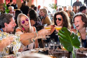 Four women toasting in crowded restaurant.