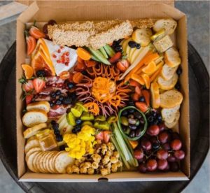 Box of fruit, meats, and cheeses for sharing.