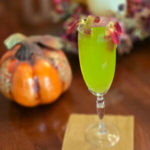 Glowing green cocktail with gummy worm on wooden table. 