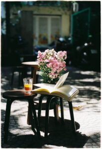 Book on an outside table with flowers and a drink