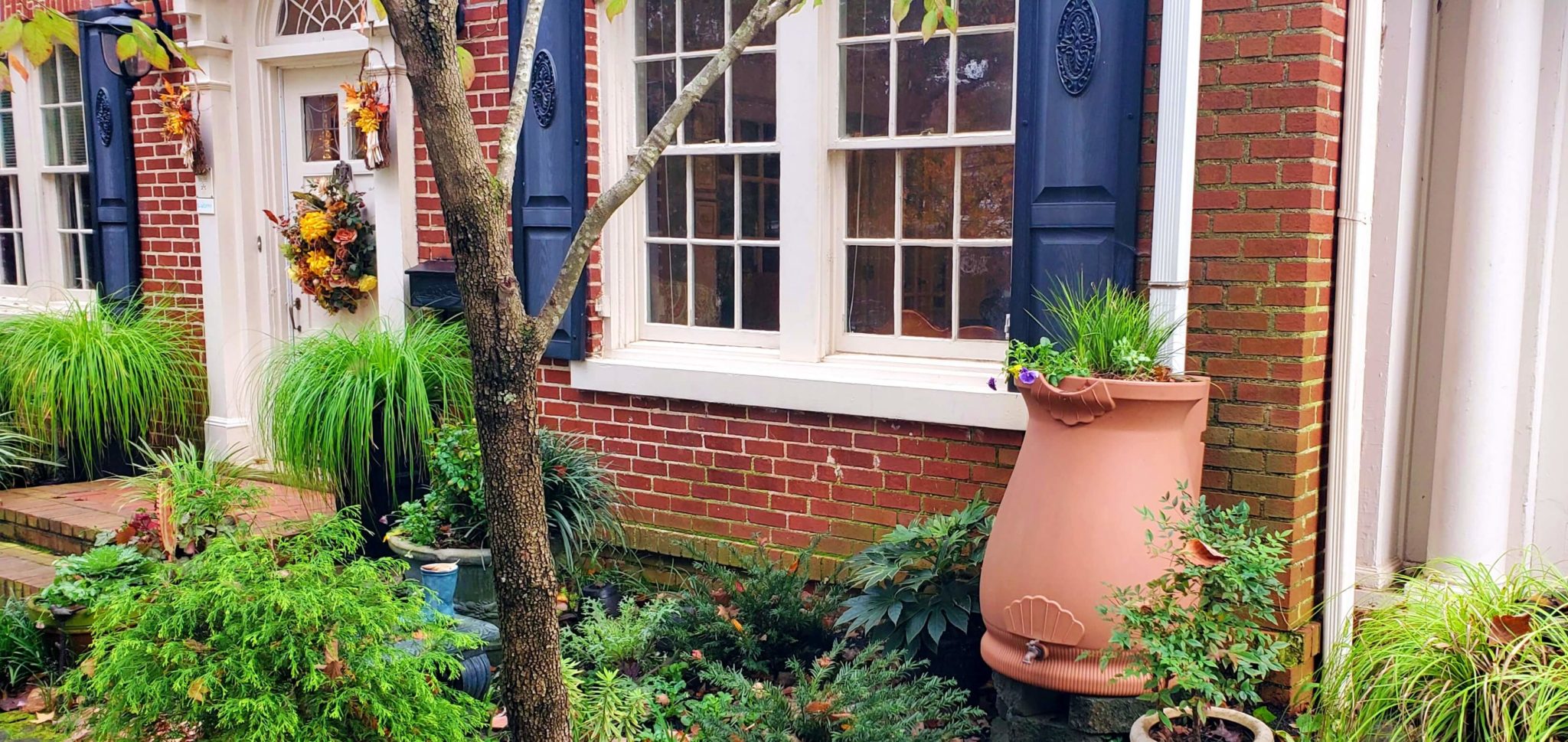 Rain water collection bucket in front of red brick house in garden.