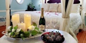 Romantic package with flickering candle tray, champagne, chocolate dipped strawberries, and silk rose petals on the bed.