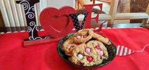 M&M cookies in green bowl on sideboard with love sign behind it.