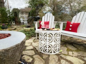 Wine and cheese tray in garden near white chairs and fire pit