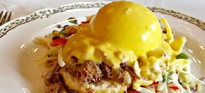 Poached egg with hollandaise sauce over biscuit on china plate.