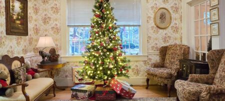 Lit Christmas tree with boxes in front of windows with two chairs