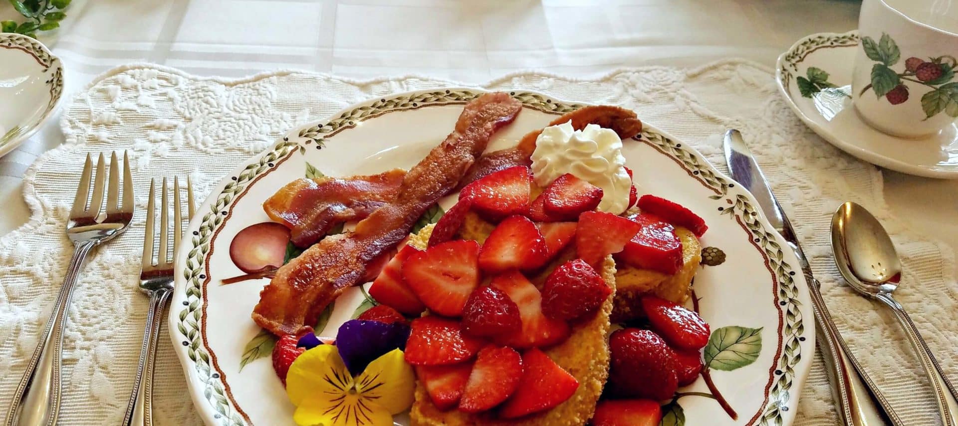 Lemonade French Toast covered in strawberries at a set table with fine china setting