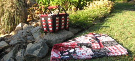 Picnic basket and blanket laid on grass by rocks.