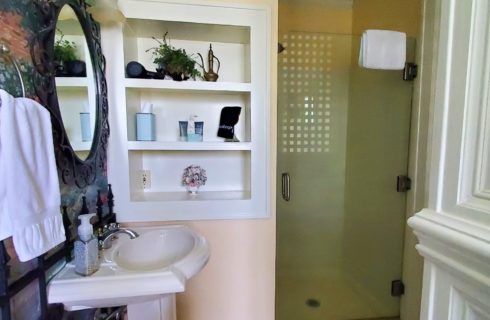 Porcelain sink, three in wall shelves, and shower stall.