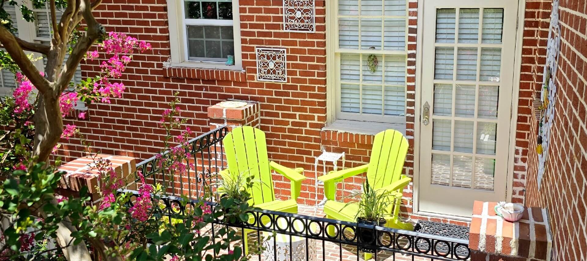 Green chairs on balcony with blooming crepe myrtle tree.
