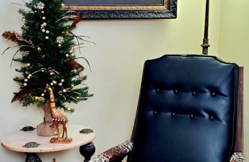 Christmas tree near antique leather chair with giraffe photo in background