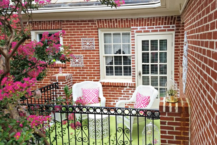 Private patio with white wicker furniture with pink and green accents.