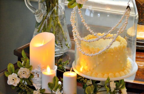 Exquisitely decorated small cake under dome decorated with pearls and surrounded with lit white candles.