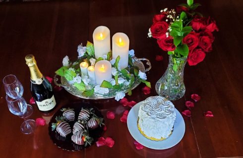 Deluxe romantic package with champagne, chocolate dipped strawberries, flickering candle tray, two-person cake, silk rose petals, and bouquet of roses.