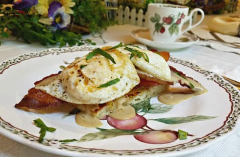 Fried eggs over ham on a china plate with a cup of coffee.