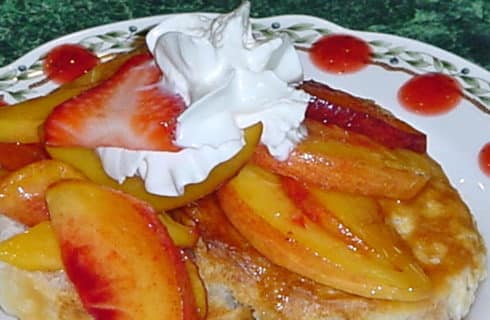 Pancakes covered with fresh paches and strawberries and whipped cream.