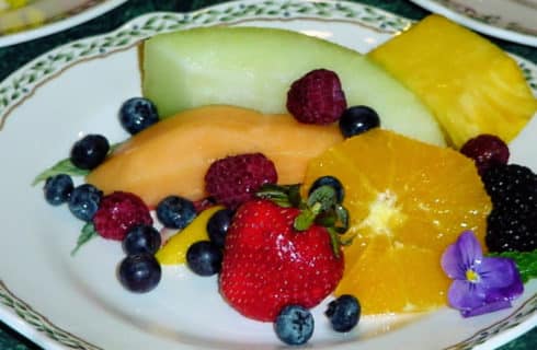 Fruit plate with melon slices, oranges and berries on a china plate.
