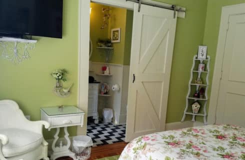 Whimisical bedroom leading to bathroom with a barn-door style door and black and white tile.