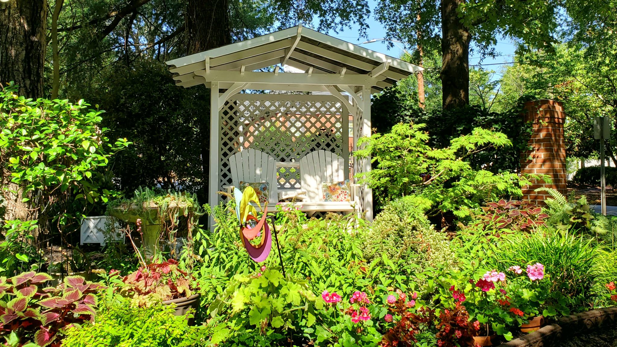 Two person glider in shaded garden with blooming flowers.