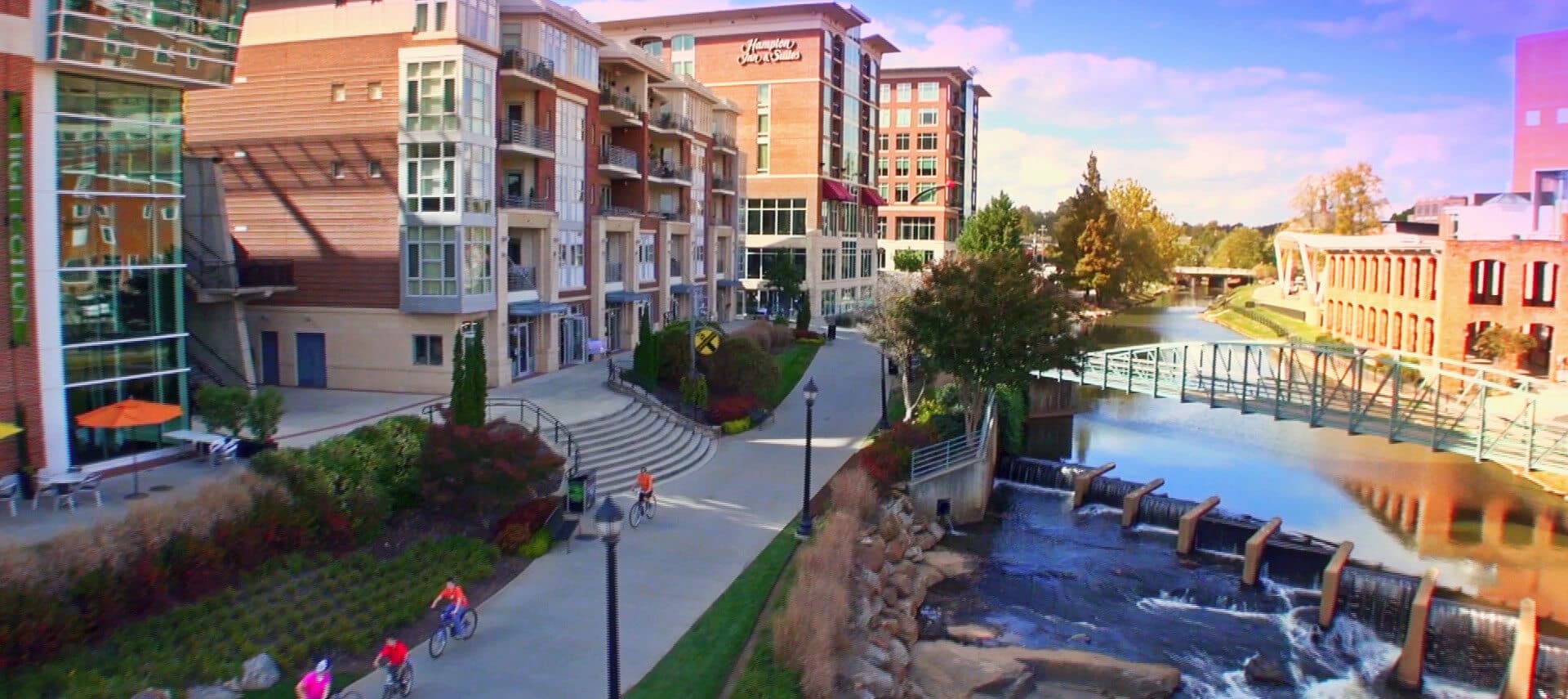 View of river from concreet walking path next to tall brick business buildings.