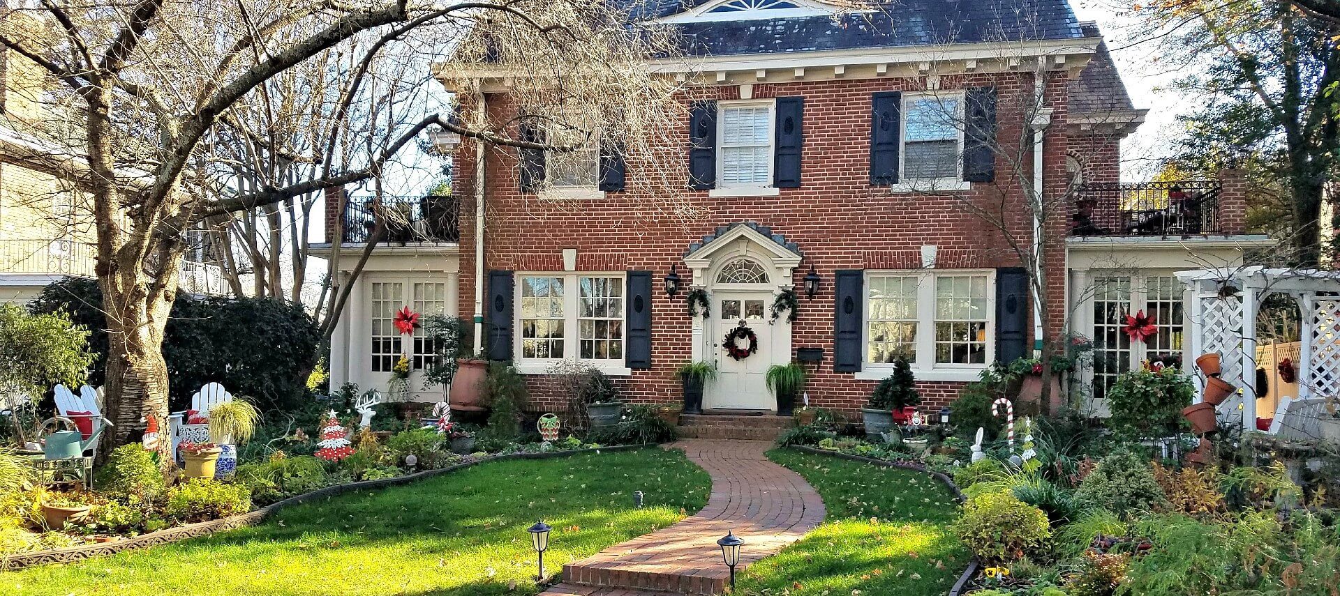 Front brick colonial house with Christmas wreath and decorations scattered around the lawn.