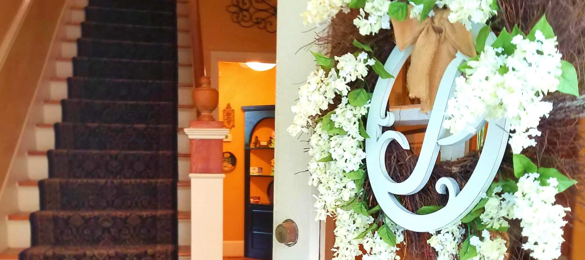 Entryway looking at staircase, with a flowered "P" wreath on the front door.