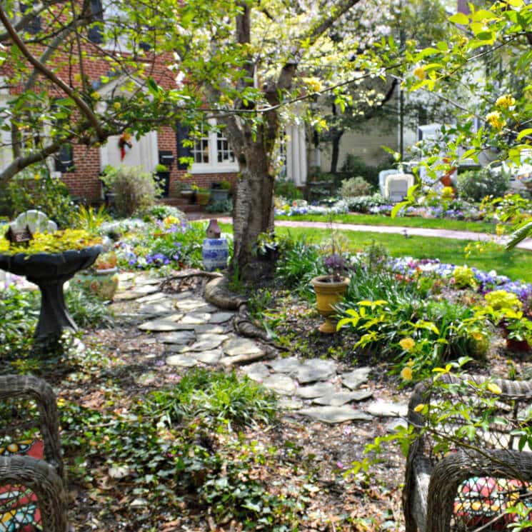 Pretty stone path winds through the trees in front of a brick Colonial.