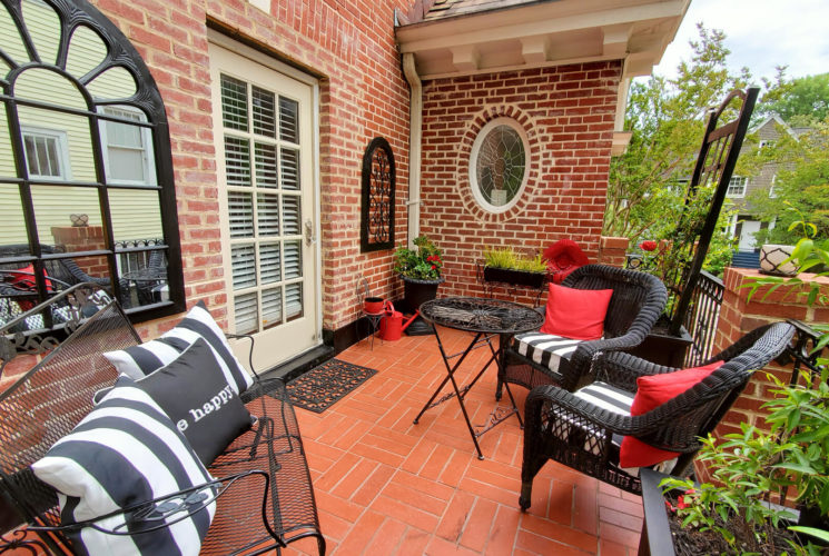 Red brick balcony with black wicker seating and pillows