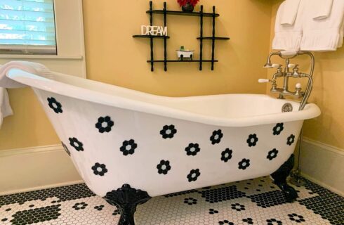 High backed claw-foot tub with black and white tiled floor in yellow room.