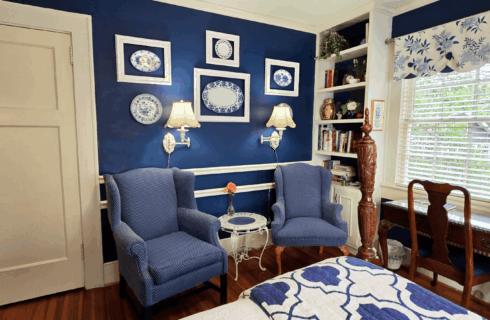 Antique high-back chairs near bookshelf with large windows.