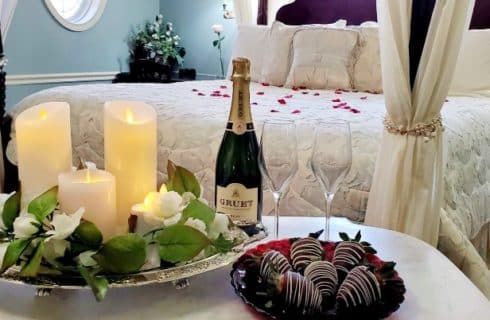 Romantic package with flickering candle tray, champagne, chocolate dipped strawberries, and silk rose petals on the bed.