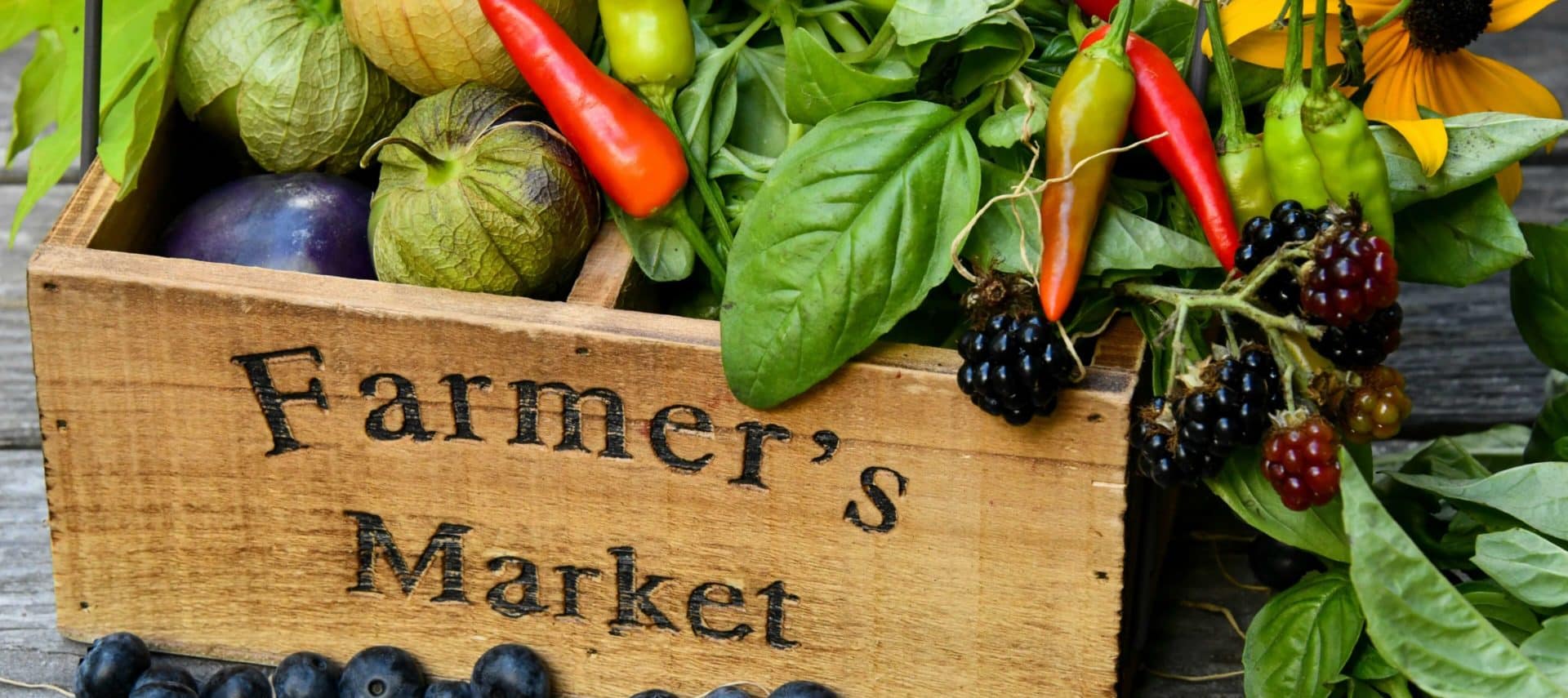 Wooden crate of fresh produce including berries and peppers.