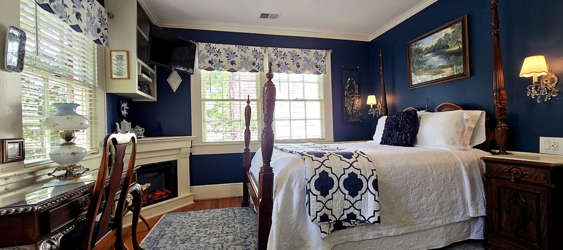 Four poster queen bed with large windows and fireplace with desk.