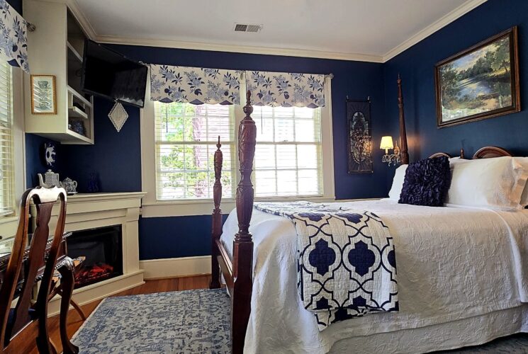 Four poster queen bed with large windows and fireplace with desk.