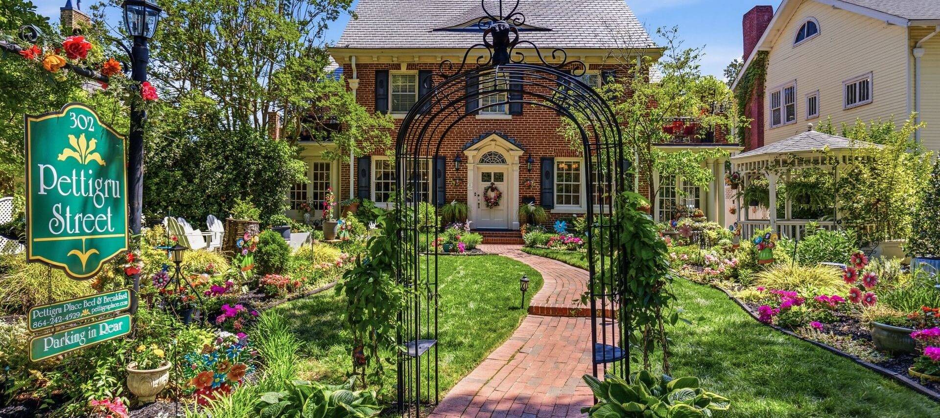 Front of red brick house with lush garden and floral arch.