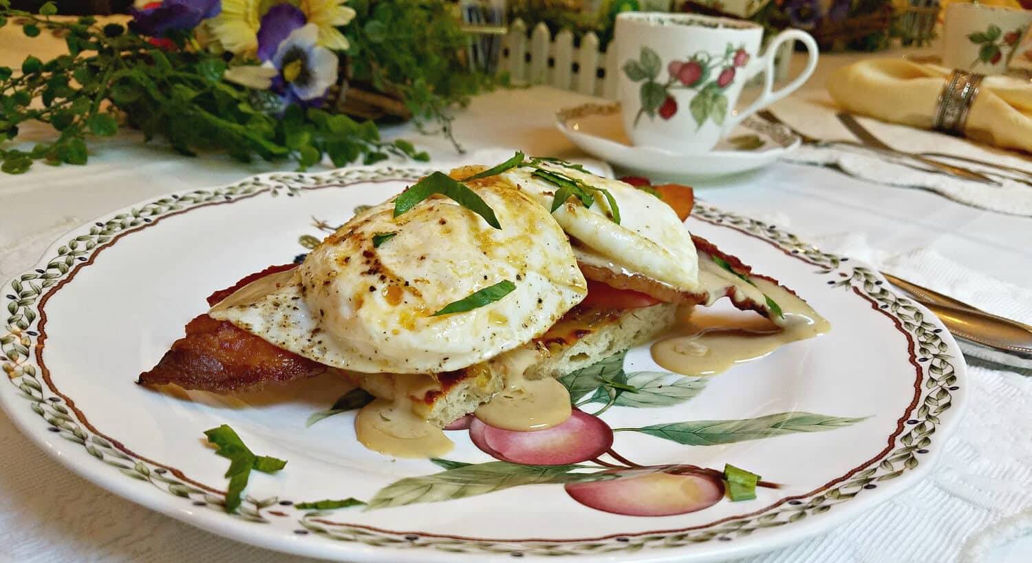 Fried eggs over ham on a china plate with a cup of coffee.