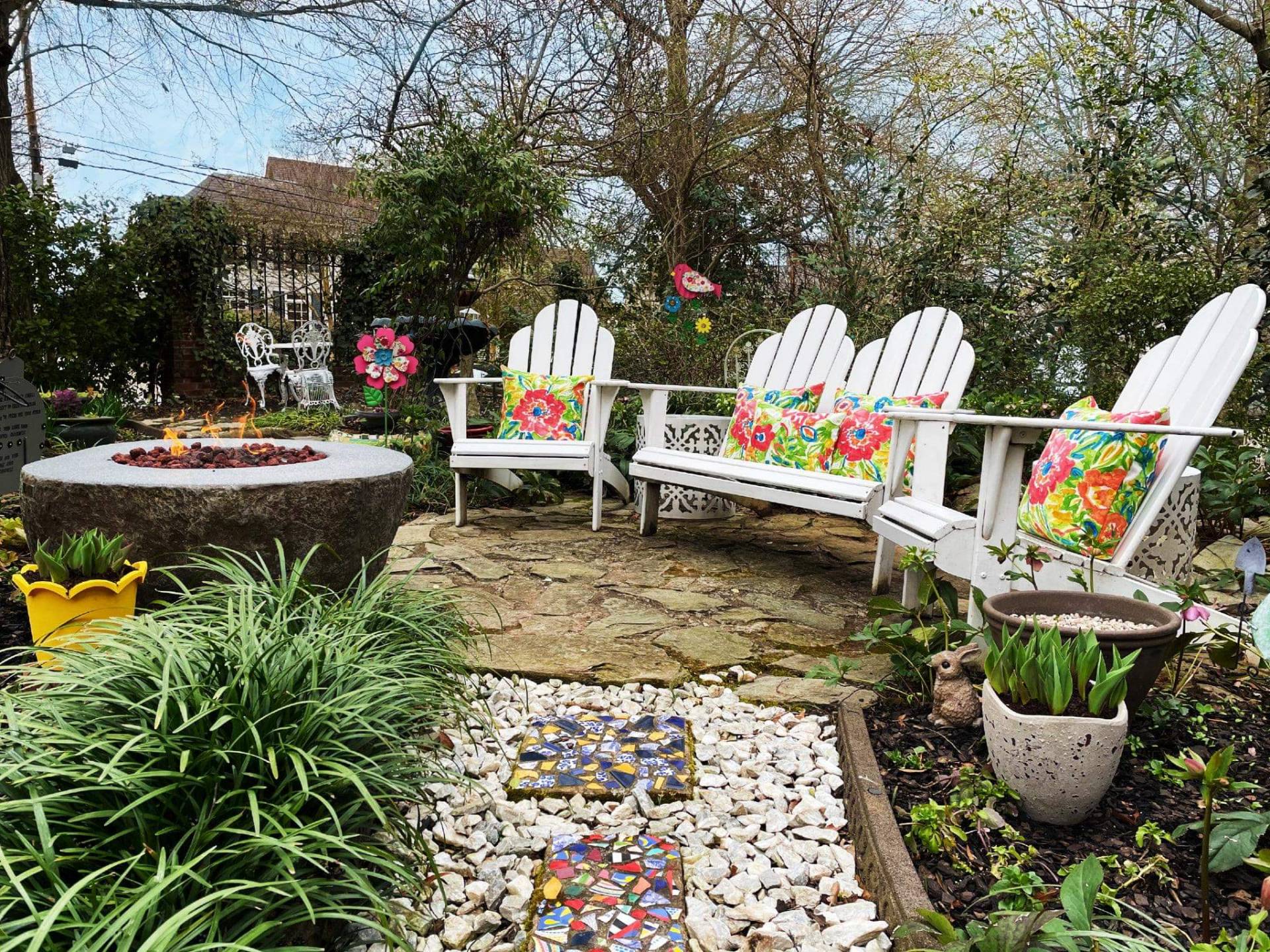 Adirondack chairs in garden on stone path with lit fire pit.