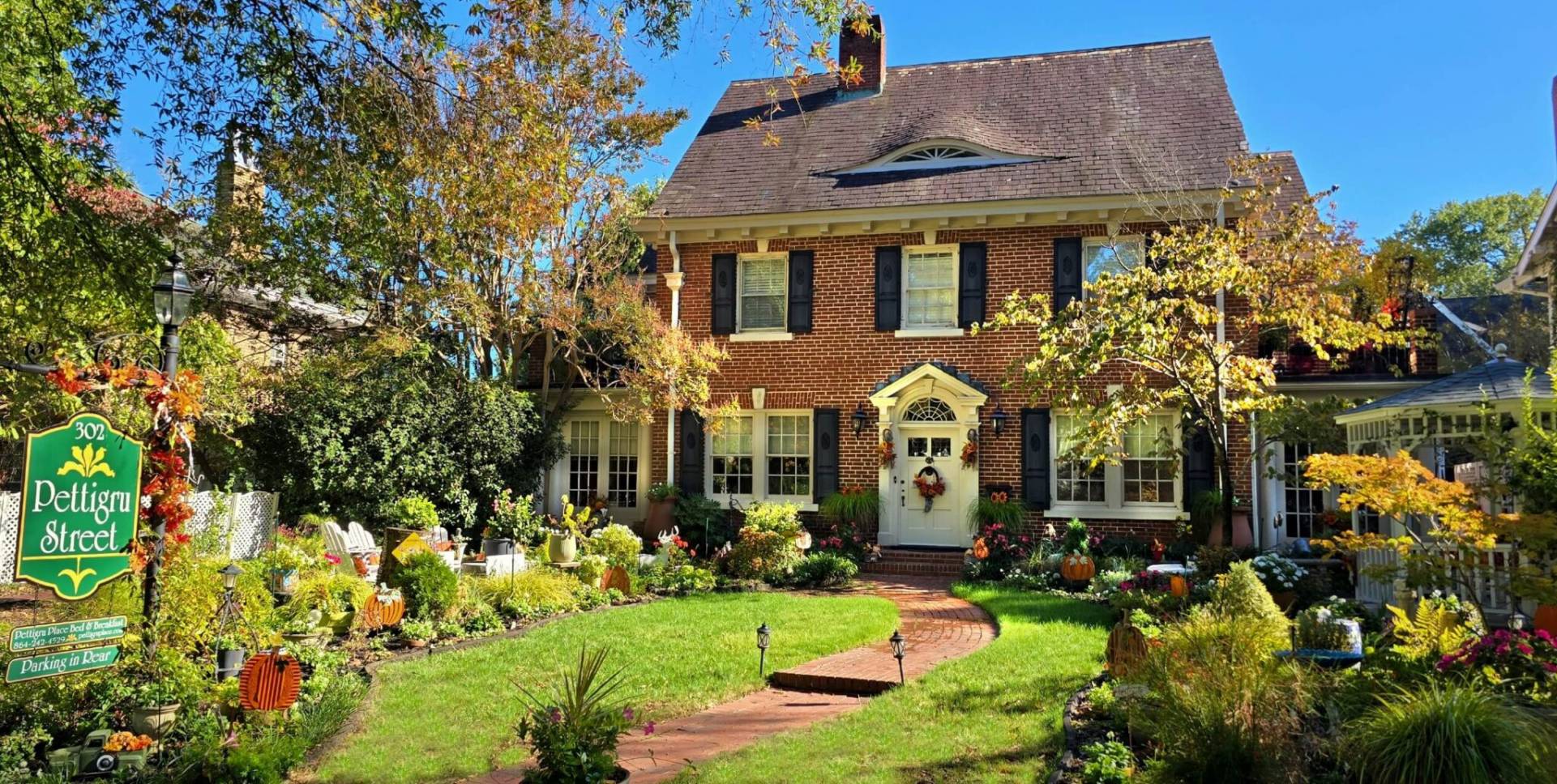 two story red brick house on sunny fall day with lush gardens