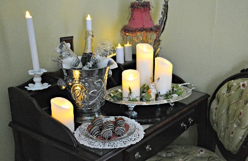 Side table in bedroom with candles, champagne in a silver bucket and chocolate covered strawberries.