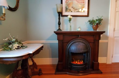 Glowing electric fireplace with flower covered mantel and side table.