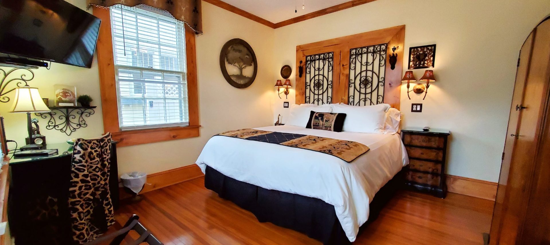 California King bed with wood and iron headboard in cream room with television and desk