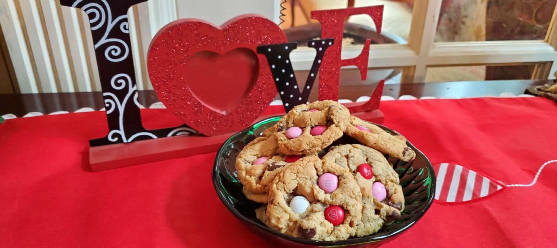 M&M cookies in green bowl on sideboard with love sign behind it.