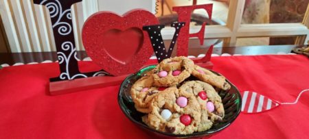 M&M cookies in green bowl on sideboard with love sign behind it.