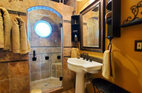 Large shower in stone archway with pedestal sink and two towels.