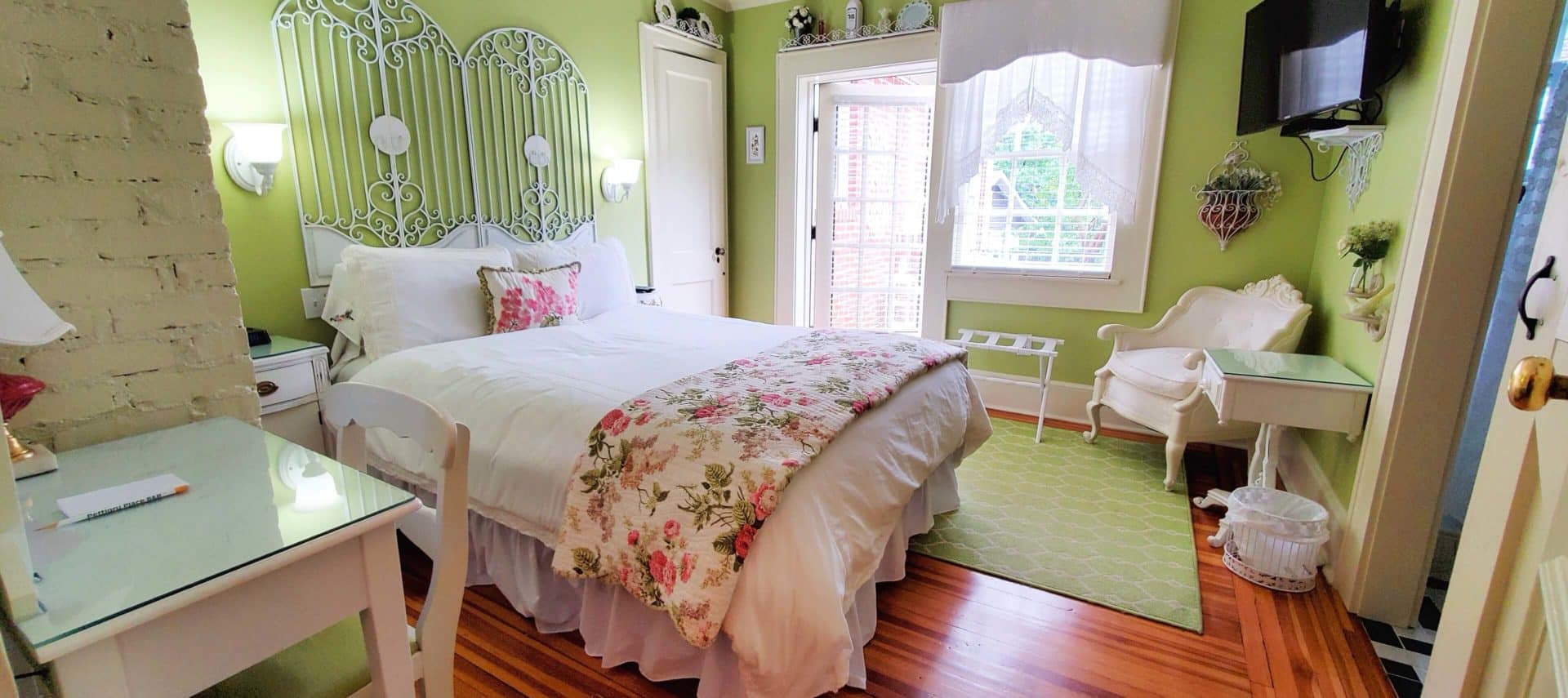 Guest room with queen bed, large screen television, desk and chair. Open patio door.