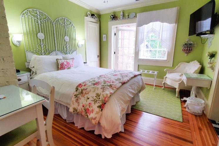 Guest room with queen bed, large screen television, desk and chair. Open patio door.